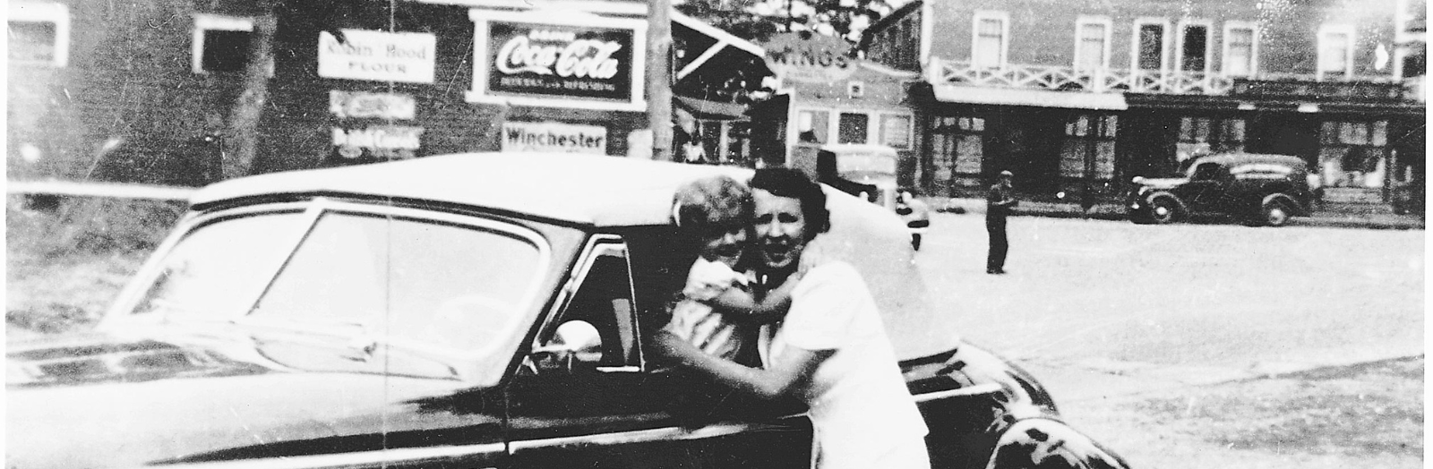 Black and white picture of a woman and a child in front of a car